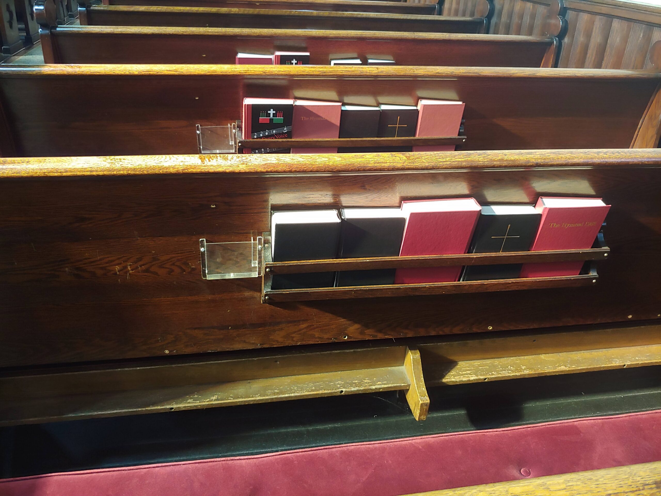 Photo of brown wooden pews and black, and red books